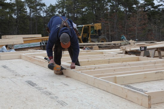 When all the full-length pieces are nailed to the bottom plate, the crew member drags the top plate over and nails it to the framing.