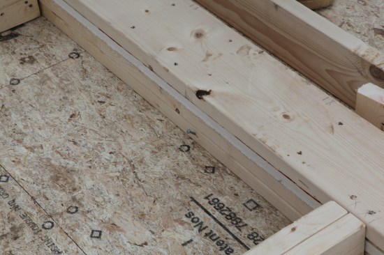 Tacks driven through the header and into the deck hold the wall square while the sheathing is nailed on.