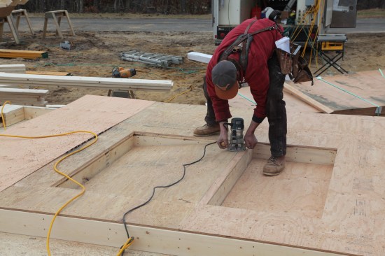 After the sheathing is tacked on, a plunge router with a bearing-guided flush-trim bit cuts out the rough openings. The sheathing is then nailed off according to schedule.