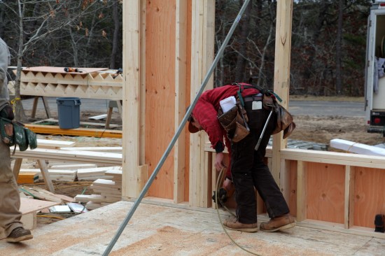 After the walls are raised, the crew makes sure the bottom plate is even with the layout line before nailing it to the deck. Two nails are driven at the base of each stud.