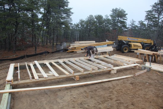 Because of the garage stem walls, there is no flat space on which to build the wall. Instead, the crew cribs up staging planks to support the top plate and sets the bottom plate on blocks next to the mudsills.