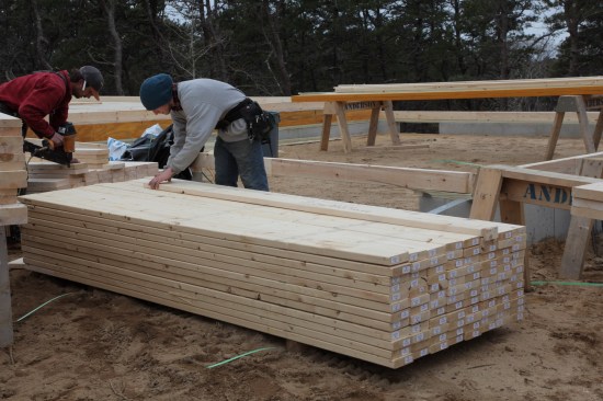 Studs for the house walls come pre-cut from the lumber supplier. But for areas such as the garage, studs have to be custom cut. Here a crew member uses a template with a stop on one end to mark the length before cutting.