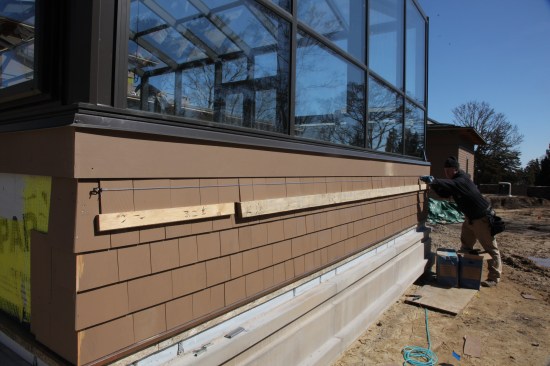 The top course has to be face nailed, so the author first slips the shingles behind the molding above and letting them rest on the ledger. Then to make sure the face nails are in a neat straight line, the author snaps a chalk line across the course from end to end.