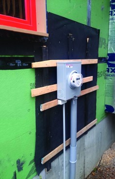 Temporary strapping the thickness of the siding holds the electric meter out from the strapping and the drainage plane until the siding can be installed.
