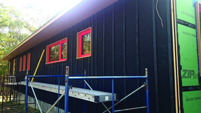 Black building paper, with 4-inch overlaps between courses, covers the side wall. To complete the drainage plane beneath the open plank siding, vertical strapping then attaches over the paper.