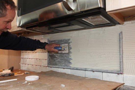 A rubber trowel beds the mural tile into the thinset and flattens the mosaic. 
