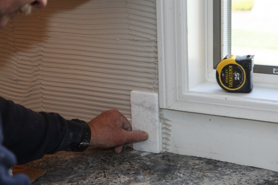 After spreading the thinset, a tile placed vertically helps to gauge the placement of the first course to leave the proper grout line along the casing.
