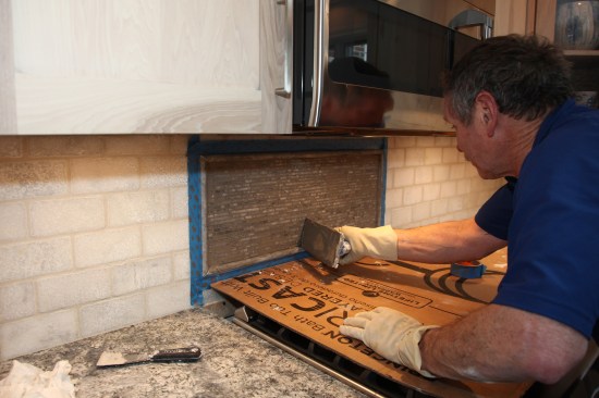 After taping around the edges of the mosaic mural, the author applies a darker color unsanded grout to the mosaics.
