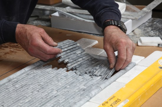 The mosaic tiles come in sheets. After cutting the sheet to fit, the author lays the the cut sheet in place to complete the dry layout.