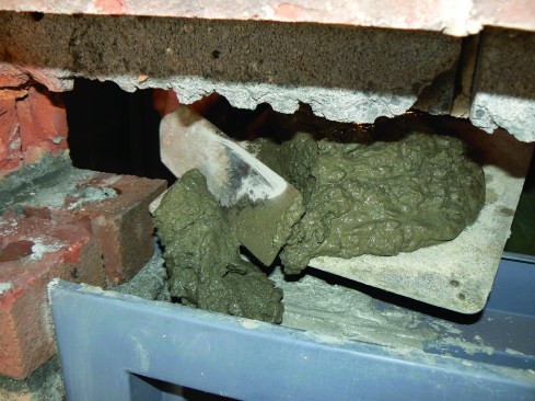 The author grouts the jamb channels from the top, scraping the mix into the header channel and pushing it into the sides.