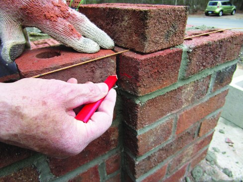 Next, he transferred the 15-inch mark to a brick set on the wall with a 3/8-inch plywood spacer to simulate a mortar joint.
