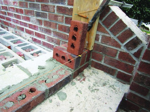 A line guided the installation of the rowlock course. To anchor the line, the author clamped a 2-by block to each side wall, looped the line over nails on the blocks, and secured the line to makeshift cleats on the faces of the blocks.