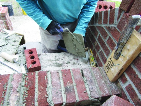 He buttered one side of the last brick with mortar and set it in place, leaving the other joint open. After spreading mortar on a hawk, he used a 3/8-inch tuck pointer to pack the final joint with mortar.