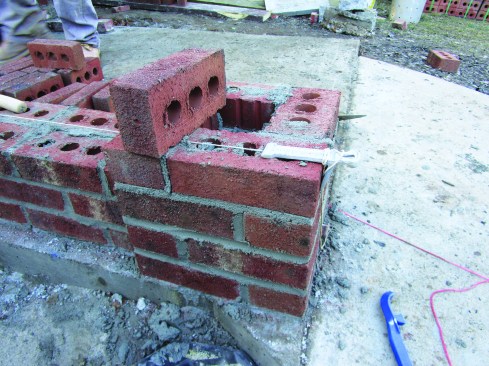 An L-shaped line block hooks over the edge of the column to hold one end of the twine while a brick holds it in line with the wall.