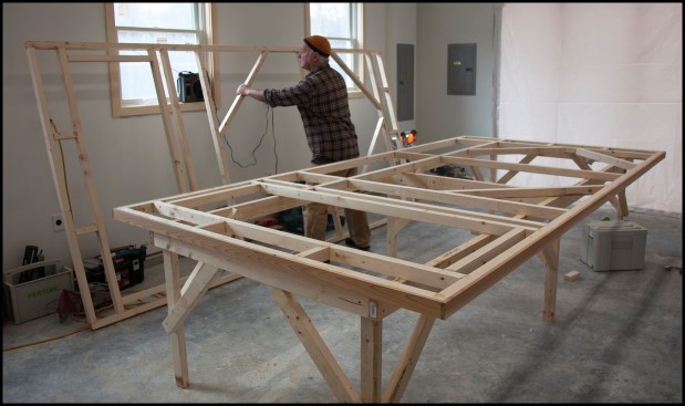 Starting with larger door pair, a temporary workbench was built the same size as the door. Dead-straight 2-by SPF lumber was selected, screwed together, and scrupulously set to a laser level line and braced to be wobble-free. Here (photo, above), the author sets aside the second assembled door grid, which was assembled directly on top of the first.