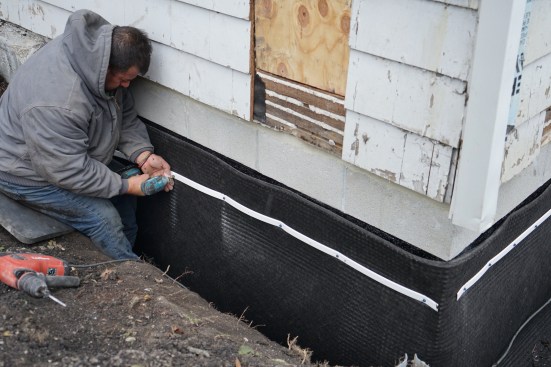 The crew next secured drainage mat to the block foundation with concrete fasteners. 