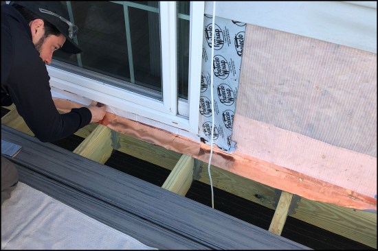 L-shaped copper flashing is installed on top of the ledger along the deck-to wall juncture. The new deck was raised 4 inches to decrease the step down from the sliding door.