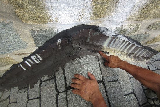 The juncture along roof cricket was repeatedly sealed with asphalt roof cement in an attempt to keep out water.