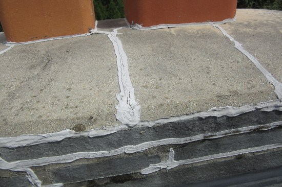Cracked concrete chimney cap heavily caulked in an attempt to keep out moisture. The mortar joints of the cap stone also heavily caulked.