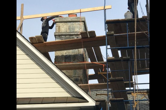 After assembling an impressive scaffold anchored to the building at multiple levels to provide lateral strength, the masons begin to remove the stone veneer and the cracked crown on the chimney.