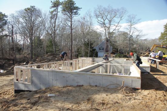 With such a long drop wall, it's important to make sure it is parallel with the foundation wall, which we confirm by measuring the distance between the rear and front walls at several places. We use 2x6s to brace the drop wall back to the steel, which we had tied to the front foundation wall earlier, providing us with a solid connection point.