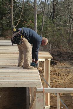 As we spread out the joists on the plates, we put them tight to the rim board on the front sections and make sure that both ends are on their layouts. Because we have no anchor bolts in the foundation, the joists can sit flat and straight, which allows us to snap a clean line along the back of the house and cut all of the joists while they're laying flat.