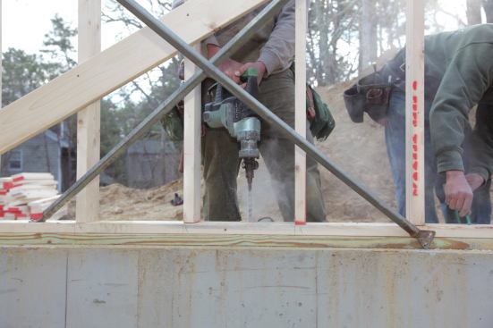 To install the anchors, one crew member drills the 5/8-inch–diameter holes through the sills and into the concrete.