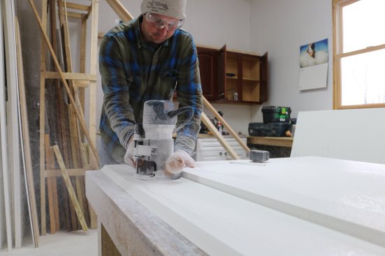 A straightedge is clamped to the layout marks on a sheet of PVC and the router follows one edge. Be sure the rotation of the bit is pushing the router table against the straightedge.