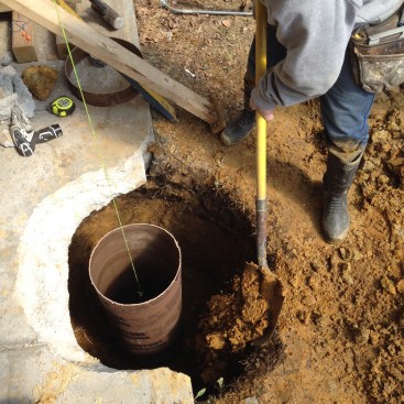 Adding backfill around the form locks it into position for the pour. A pump keeps water out of the footing until the concrete can be poured.