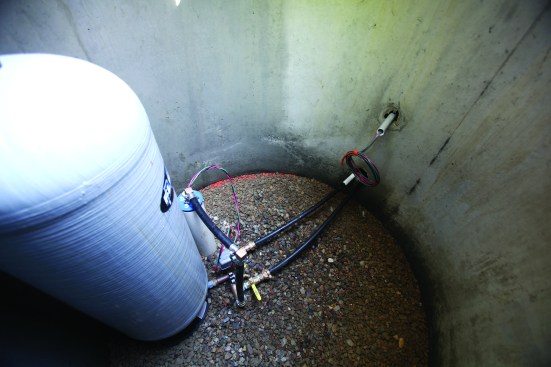 Water lines exit and power supplies enter through knock-outs in the wall of the well pit. The ambient earth temperature keeps the well, supply pipes, and pressure tank from freezing.