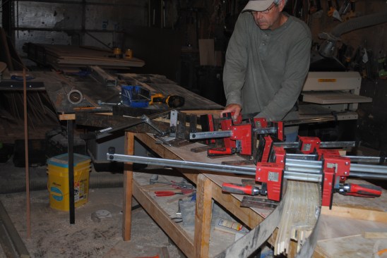 This glue up creates the both the top rail and the curved panel molding for the back panel so the authorglues up both pieces at once. After applying glue to each set of strips (with a dry layer between the two sets) and he places them together in the jig for the glue-up. 