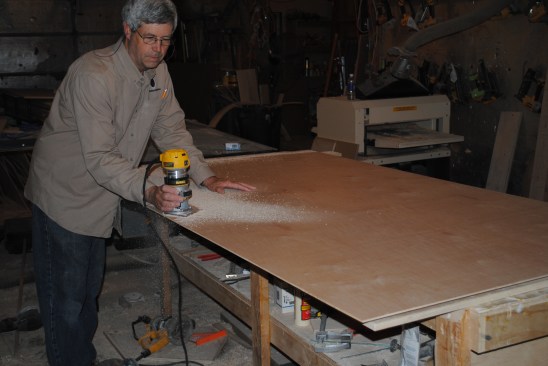 After gluing and nailing the plywood back into place, the author uses a small router with bearing-guided bit to remove the excess material from around the frame.
