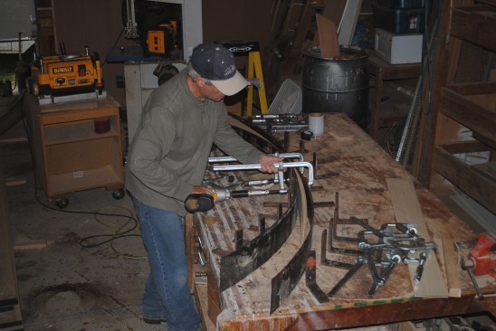 Angle irons screw to the radius for the curve that the author had drawn on the bench top. Thin pieces of steel sandwich the strips into the shape of the curve.