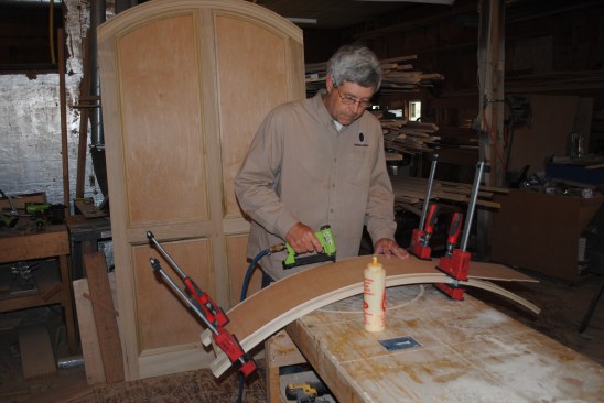 The 14-inc plywood back is flexible enough to bend over the curved top. After applying glue to the frame, the author staples on the back, using clamps to hold the plywood to the frame.