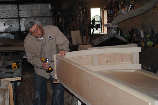 Holding the side on the square mark he just made, the author screws the top to the side panel.