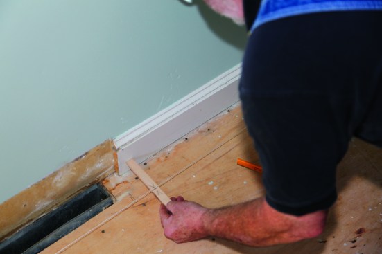 After checking the walls for parallel, a string is stretched along the beginning wall. A simple piece of wood with the distance marked on it becomes a gauge to see how straight the wall is and to find the farthest point from the string.