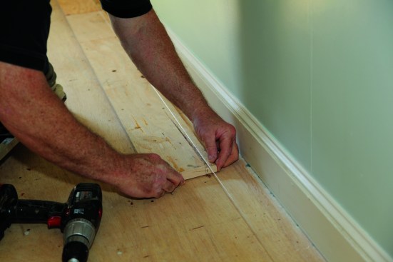 A straightedge screwed to the floor will keep the starter course straight as it's being scribed to the wall. A notched stick helps place the straightedge precisely parallel to to the string.