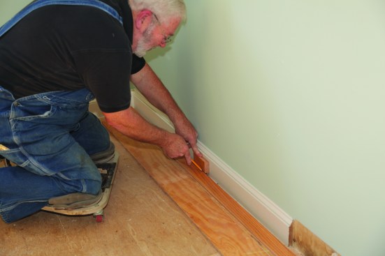 After cutting the first course to length and setting it against the straightedge, a scrap piece of flooring is used to mark the scribe line.