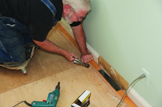 A nail spinner (in the drill on the floor) drives the flooring nails part way. A hammer finishes driving them and each nail is set flush with the tongue.