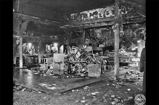 Here, the main dining room and dance floor as seen after the fire. A retractable roof located over the dance floor was closed for the winter, its opening concealed by a suspended cloth ceiling below. The flammable satin ceiling—which stretched wall to wall—contributed to the rapid speed of the fire across the grade-level rooms.