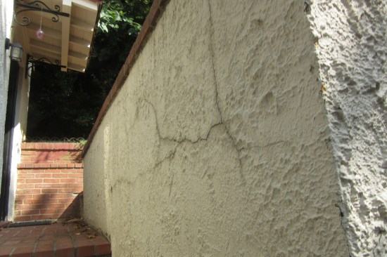 The top of the stucco-clad façade was cracked in numerous places and showed signs of multiple repairs over the years (repairs made as a result of the structure being slowly “pushed” downhill).