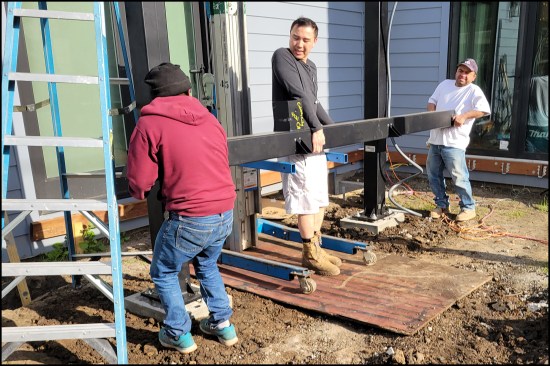 Figure 3A. The homeowner (at center in photo) helps wrangle the first beam into place with the help of a Genie lift.