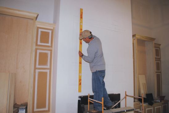 Marks are transferred from a story pole to lay out the upper mantel on the wall above the fireplace.