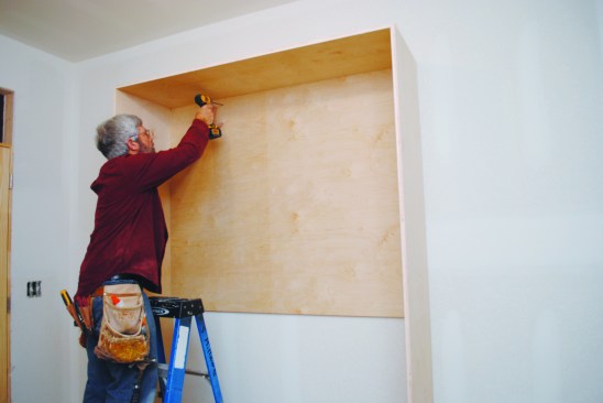For racking strength, I added a piece of 3/4-inch plywood for the upper back, and ripped a narrower width of 3/4-inch plywood and installed it at the bottom. Then I stood the cabinet up, centered it on the wall, and screwed it into place.