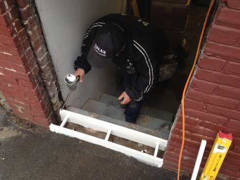 After drilling and inserting rebar to connect the concrete curb  to the step below, Silva uses spray foam to lock the form into place for the pour. A coat of bonding adhesive on the old concrete will help bond the curb in place.