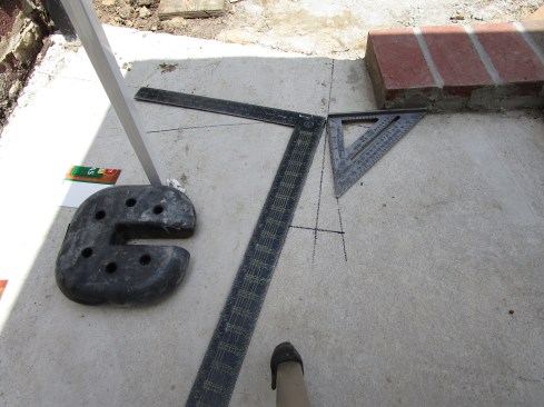 After running the border bricks to within one brick width of the flare in the walkway, the author draws a layout line for the bricks along the flare’s border. Then he uses squares to lay out the angle of the bend, and he bisects this angle to define the cut angle for the bricks.
