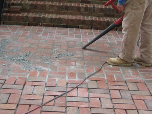 A leaf blower blows the dried mortar off the walkway. Using a broom that can smear the mortar into the surface of the bricks should be avoided.