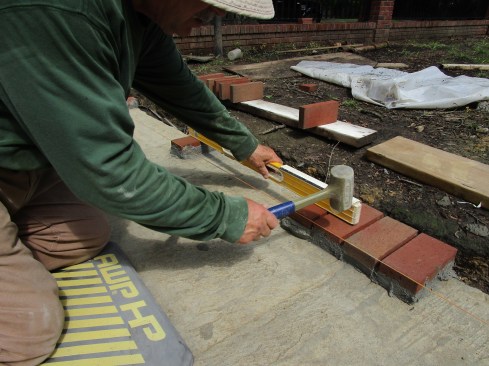 The author adds a brick next to his first group and taps it into place, leveling over to the next brick in the sequence 