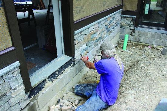 To create a solid toekick below each door, the crew cuts slabs of Pennsylvania bluestone to fit each spot. They remove any chunks of mortar left behind from installing the veneer.