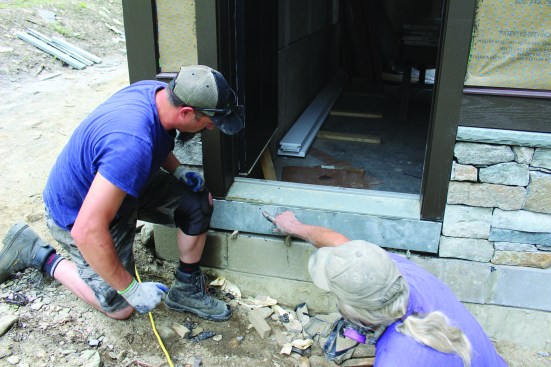 After pushing the stone tight against the door threshold, they slip in temporary wedges to hold the toekick in place until the mortar sets.